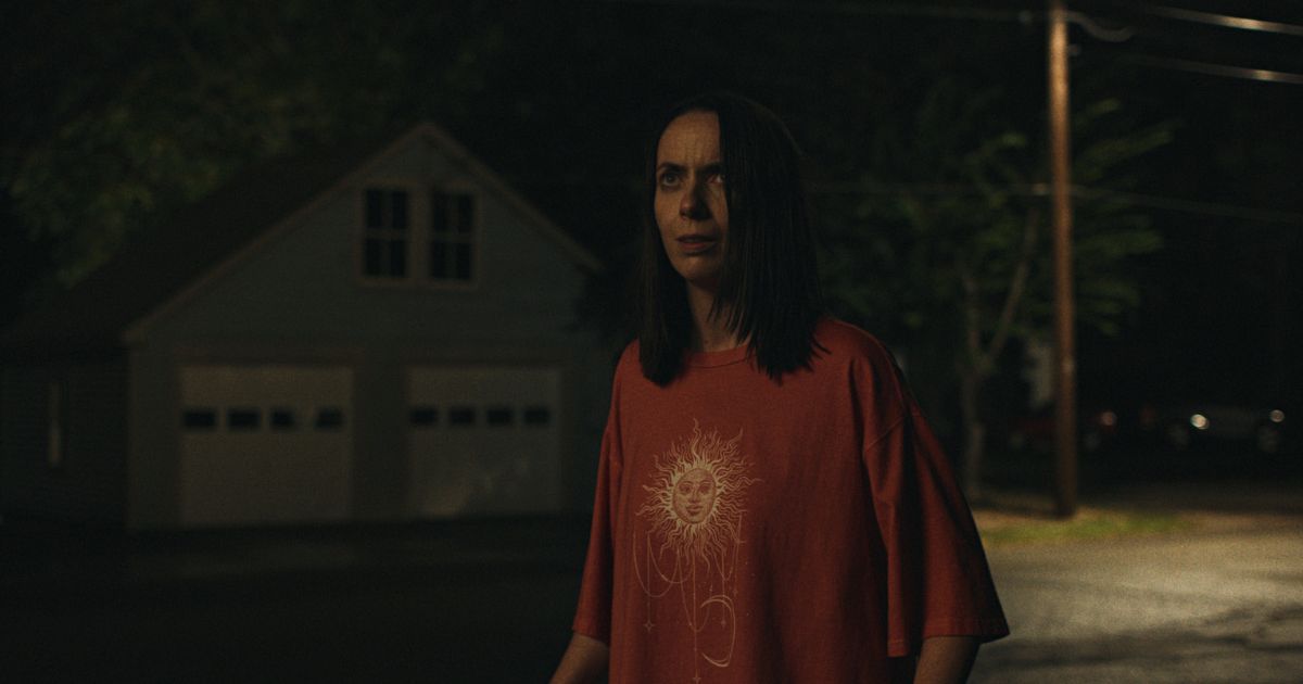 woman in orange tshirt outide in evening looking upwards