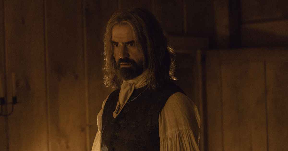 man with beard and long hair in period clothes looking serous
