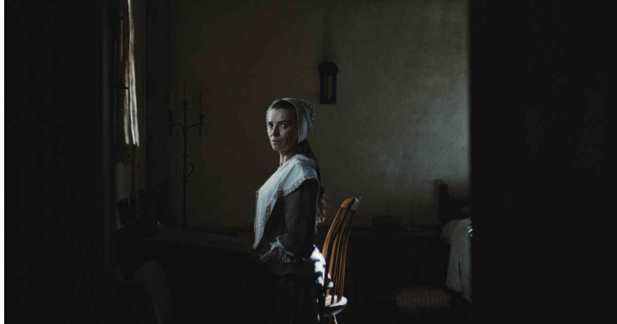woman in hat and period clothes sitting on chair in dar